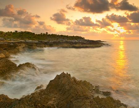 Caribe Maya view of the water and rocks at sunset with the sky a golden color in mexico